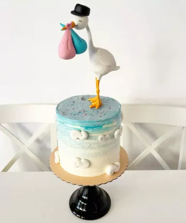 Tarta con una cigüeña que lleva en el pico dos bolsas, una azul y otra rosa